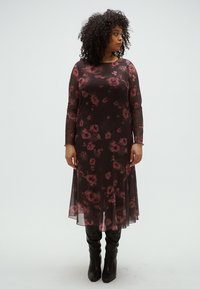 Rochie lungă, neagră și transparentă cu imprimeu floral roz închis, mâneci lungi și tiv fluid, asortată cu cizme negre până la genunchi.