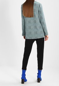 Rutig kavaj i teal och svart, kombinerad med svarta snäva byxor. Blå klackade ankelskor fulländar stilen. Tydlig bakvy.