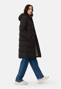 Black puffer coat with a hood, featuring a zip closure and side pockets, worn over blue wide-leg jeans and light-colored sneakers.