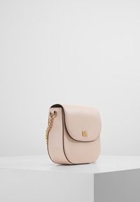 Rosa læder crossover taske med flaplukning, prydet med en guld kædedyse og præget logo, glat tekstur og rund form.