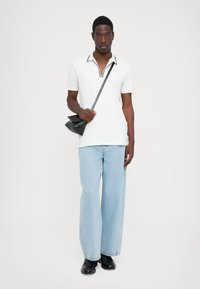 Hvit polo skjorte for menn med stripet krage, kombinert med lyseblå vide jeans og svarte sko, bærer en liten svart veske.