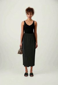 Black ribbed tank top paired with a long black pleated skirt. Model holds a brown handbag and wears black slide sandals.