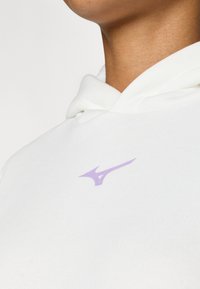 Hanorac alb cu o textură moale, cu glugă ajustabilă și un mic logo violet pe partea stângă a pieptului.