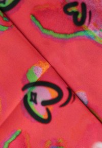 Tessuto colorato con uno sfondo rosso e forme di cuori astratti e linee in nero, verde e rosa, con una texture liscia.