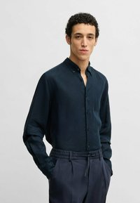 Granatowa koszula z długim rękawem z kołnierzykiem zapinanym na guziki, wykonana z lekkiego materiału. Połączona z granatowymi spodniami z elastycznym paskiem.