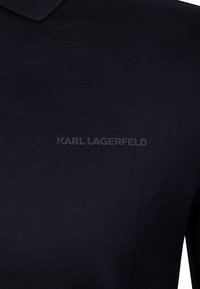 Czarna koszulka polo wykonana z miękkiego materiału; posiada klasyczny kołnierzyk oraz wyraźne logo "KARL LAGERFELD" w kontrastującym, teksturowanym tłoczeniu.