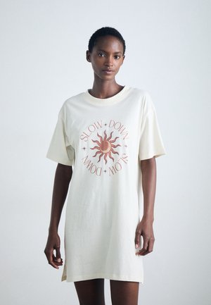 Krämfärgad oversized t-shirt klänning i bomull, med en grafik av solen och texten "SLOW DOWN" i rostfärgad bokstäver.