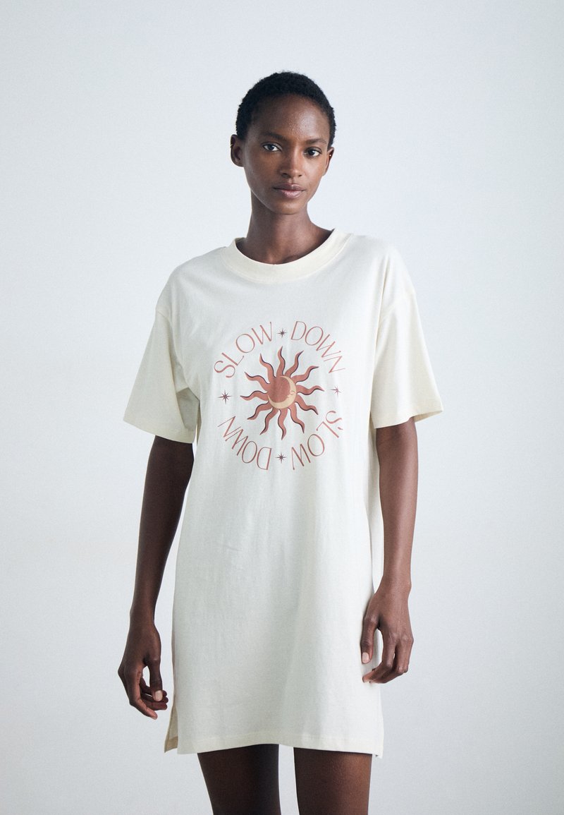 Cream-colored oversized t-shirt dress made of cotton, featuring a sun graphic and the text "SLOW DOWN" in rust-colored lettering.