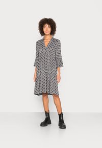 Robe noire et crème à motif avec des manches évasées et un décolleté en V, associée à des bottines noires. Tissu doux avec une silhouette fluide.