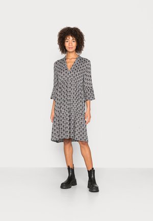 Robe noire et crème à motif avec des manches évasées et un décolleté en V, associée à des bottines noires. Tissu doux avec une silhouette fluide.