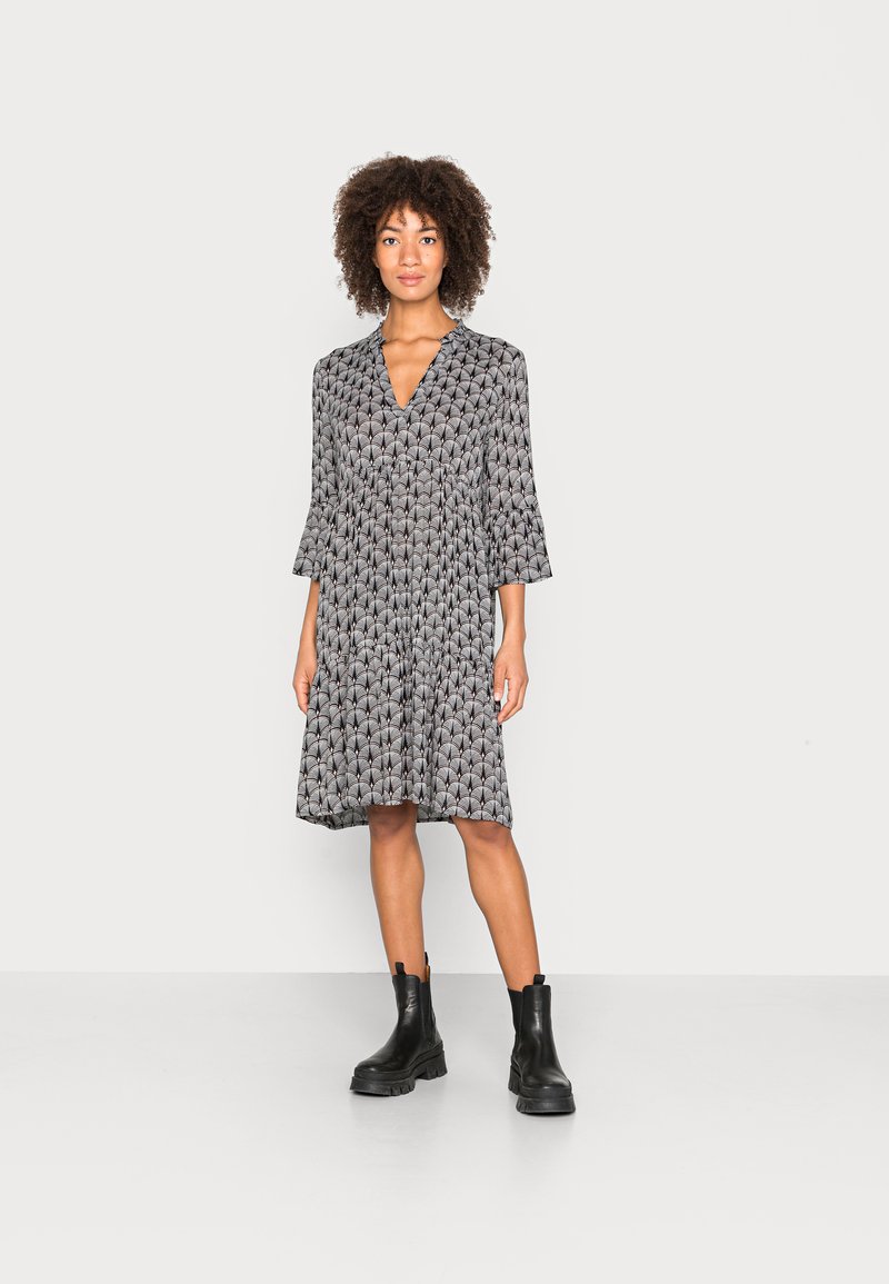 Robe noire et crème à motif avec des manches évasées et un décolleté en V, associée à des bottines noires. Tissu doux avec une silhouette fluide.