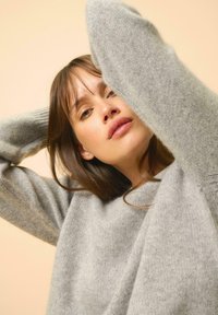 Pull gris clair en matière douce avec une coupe décontractée, doté de manches longues et d'un col rond simple, le tout sur un fond neutre.