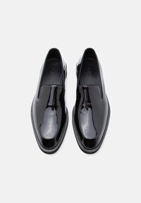 Fekete, fényes bőr slip-on cipők lekerekített orral, sima textúrával és rugalmas oldalpanellel. Jellemzője egy lapos fekete gumitalp.