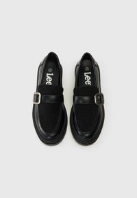 Fekete slip-on cipők velúrviasz és bőr felülettel, széles pánttal és ezüstcsat részlettel. Kerek orr és texturált talp.