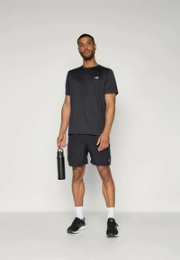 Camiseta y pantalones cortos deportivos negros hechos de material que absorbe la humedad. La camiseta tiene un logo pequeño; el modelo sostiene una botella de agua negra.