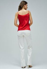 Camisola de satén roja con tirantes finos, combinada con pantalones blancos de pierna ancha, mostrando una textura suave y líneas limpias sobre un fondo neutro.