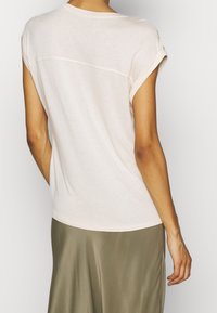 Light pink relaxed-fit t-shirt with rolled sleeves, featuring a smooth texture and a subtle back seam. Paired with an olive green skirt.