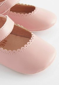 Pink leather Mary Jane shoes with scalloped trim and strap, rounded toe, and smooth texture. Inner lining is light brown.