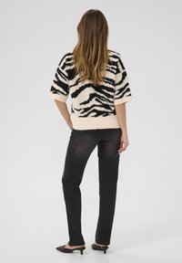 Women’s short-sleeve fuzzy sweater in cream with black zebra stripes, paired with dark denim jeans and black pointed-toe flats.