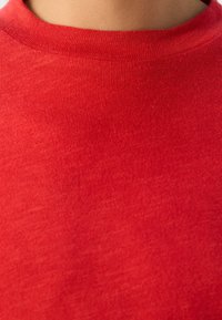 Tessuto di cotone rosso con una fine trama arricciata, caratterizzato da un collo rotondo. La vista ravvicinata evidenzia la superficie liscia e uniforme.