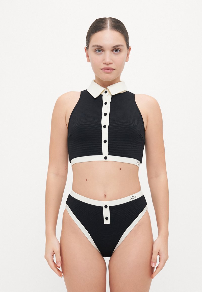 Black two-piece swimwear set featuring a collared crop top with button details and high-waisted bottoms with contrasting cream accents.