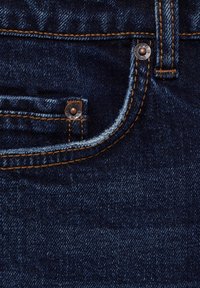 Pantalones vaqueros de mezclilla azul oscuro con costuras visibles, un pequeño bolsillo delantero y remaches metálicos. La tela tiene una textura suave.