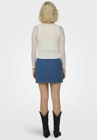 Maglia bianca a maniche lunghe con coste abbinata a una gonna di jeans blu. Stivali da cowboy neri visibili. Design semplice e aderente senza ulteriori decorazioni.