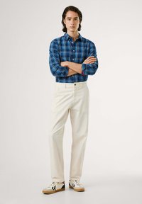 Blauwe geruite overhemden, ivoorkleurige broeken en witte sneakers met zwarte en rode accenten. Glad materiaal, relaxte pasvorm, casual stijl.
