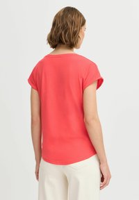 Korallefarbenes T-Shirt mit kurzen Ärmeln und Rundhalsausschnitt, aus weichem Baumwollstoff und lockerer Passform, kombiniert mit hellen Hosen.