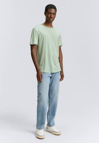 Hellgrünes T-Shirt mit kurzen Ärmeln in lockerer Passform, kombiniert mit hellblauen Jeans mit geradem Bein und weißen Sneakers mit beigen Akzenten.