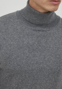 Grå turtleneck sweater lavet af blødt strikmateriale. Har en høj ribbet krave og en tekstureret overflade med fine, subtile prikker overalt.
