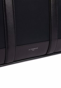 Borsa nera in pelle con finitura texturizzata, caratterizzata da accenti lisci e un logo metallico. Forma strutturata con dettagli di cucitura visibili.