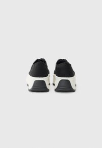 Svarte overdel sneakers med hvit mellomsåle og svart yttersåle. Rund form med glatt tekstur, med minimal detaljering.