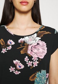 Svart blommig kortärmad topp med stora rosa och ljusblå blommor samt gröna blad, rund halsringning och mjuk tygstruktur.