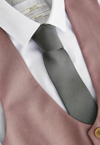 Gilet rose clair avec une cravate grise texturée, associé à une chemise blanche. Comprend un détail de bouton et un motif de tissu subtil.