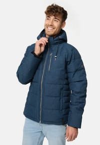 Parka u mornarsko plavoj boji s kapuljačom, zatvaranjem na patentni zatvarač i kviltanim dizajnom. Materijal izgleda teksturirano, s malim logotipom na rukavu.