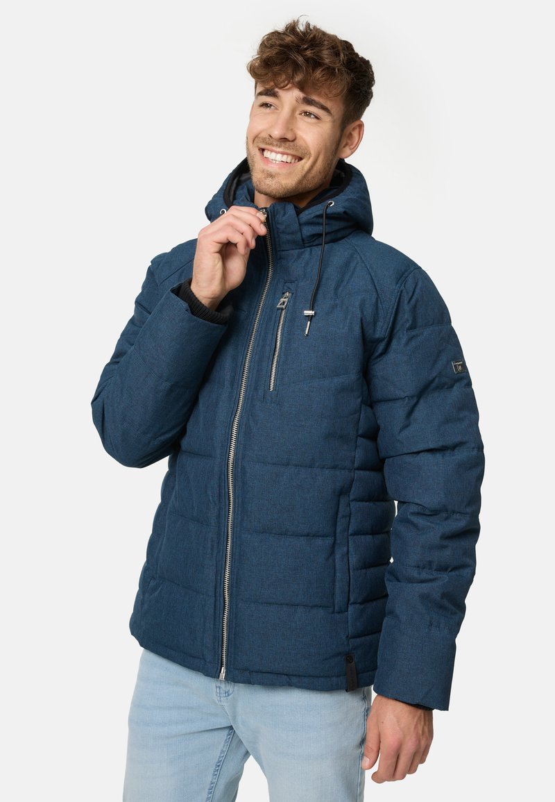 Parka u mornarsko plavoj boji s kapuljačom, zatvaranjem na patentni zatvarač i kviltanim dizajnom. Materijal izgleda teksturirano, s malim logotipom na rukavu.