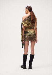 Hedvábný top s šátkem a mini sukně v béžové barvě s tmavými tištěnými vzory. Stylizováno s černými vysokými botami. Hladká textura a obepínající design.