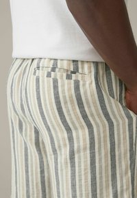 Pantalons en lin rayés avec des rayures verticales beige clair et gris, dotés d'une poche arrière et d'une coupe ample.