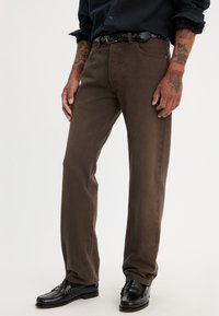 Pantalones rectos marrones hechos de algodón, con un diseño clásico de cinco bolsillos y combinados con mocasines negros de cuero.