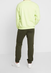Ljust grön sweatshirt med sänkta axlar och ribbade manschetter, ihopparad med mörkgröna joggers. Vita sneakers fulländar outfiten.