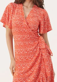 Rotes Wickelkleid mit einem weißen abstrakten Muster, flatternden Ärmeln und einem Gürtel in der Taille, mit einem fließenden Textileffekt.
