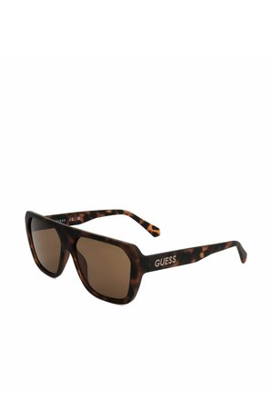 Occhiali da sole Guess con motivo tartarugato, lenti quadrate marroni e logo sulla stanghetta, esposti su sfondo bianco semplice.