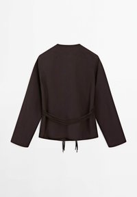 Veste noire à manches longues avec un col rond et un détail de ceinture à la taille, vue de dos sur un fond blanc.