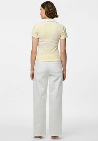 Camiseta polo a rayas en amarillo pálido y blanco, de manga corta, con un cuello; combinada con unos pantalones vaqueros blancos de pierna ancha y cintura alta.