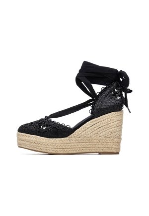 Cuña de esparto negra tejida con suela de yute, que presenta un diseño de cordones y detalles intrincados en la parte superior.