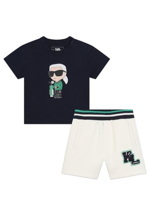 T-shirt in cotone blu navy con design grafico, abbinato a pantaloni corti bianchi con vita a righe e patch con logo. Tessuto morbido, stile casual.