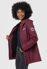 Giacca bordeaux con cappuccio, chiusura con zip frontale e fodera rossa. Presenta un logo ricamato sulla manica e tasche per le mani con zip.