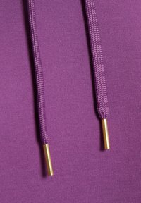 Tissu de sweat à capuche violet à texture lisse, doté de cordons tressés avec embouts en métal doré. Vue rapprochée mettant en valeur les détails.