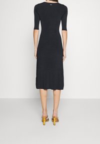 Robe noire côtelée jusqu'aux genoux avec des manches courtes, dos en forme de scoop et design ajusté. Associée à des sandales à talons blocs jaunes.